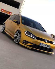 a yellow vw golf gtr parked in front of a white building with black rims