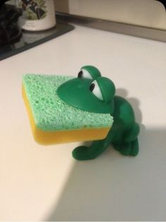 a toy frog holding onto a sponge on top of a counter