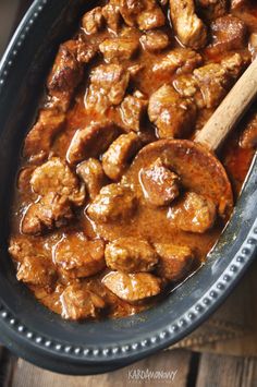 meat and sauce in a black bowl with a wooden spoon on the table next to it