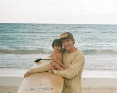 a man holding a young boy on top of a surfboard near the ocean's edge