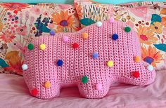 a pink knitted elephant pillow sitting on top of a bed covered in pom poms