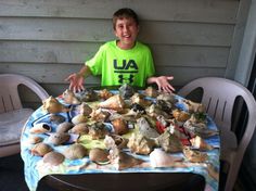 a young boy sitting at a table covered in rocks and seashells with his hands out