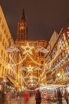 people are walking around in an old european city at christmas time with lights and decorations on the buildings