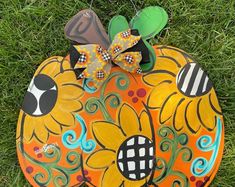 a painted pumpkin sitting in the grass with a bow on it's head and eyes