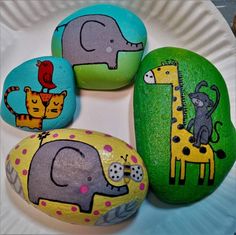 four painted rocks with animals on them sitting on a plate next to another rock that has an elephant, giraffe, and zebra