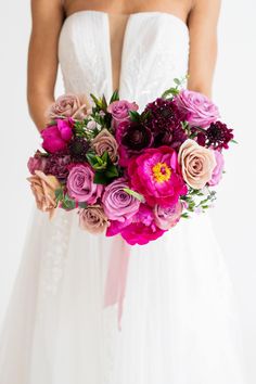 a bride holding a bouquet of pink and purple flowers on her wedding day in front of a white background