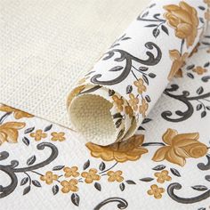 a white and gold floral wallpaper with black, brown, and yellow flowers on it