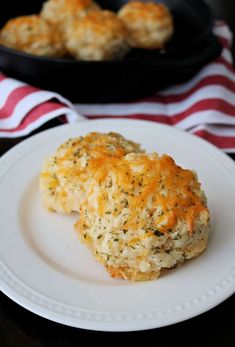 a white plate topped with biscuits next to a skillet filled with cheese and herbs