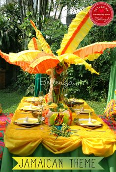 the table is set with yellow cloths and orange paper umbrellas for an exotic theme