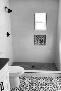 a black and white photo of a bathroom with tile flooring, shower stall and toilet