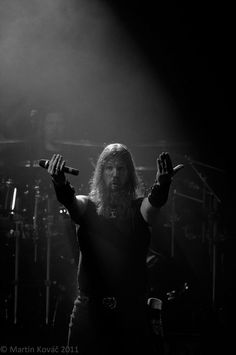 a man with long hair and beard holding his hands up in the air while standing on stage