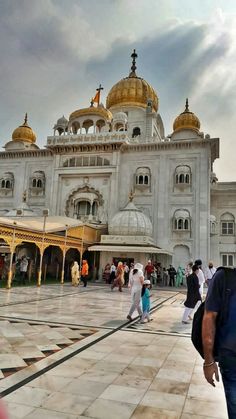 people are walking around in front of a large white building with gold domes on top