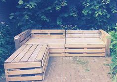 a wooden bench sitting on top of a brick floor next to green plants and bushes