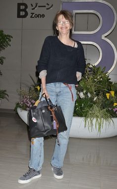 a woman holding a black purse standing next to a planter with flowers in it