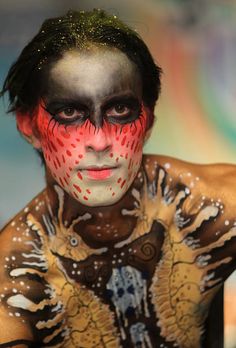 a man with painted face and body is posing for the camera while holding his hand up to his head