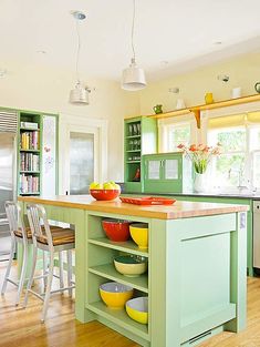 a kitchen with green cabinets and yellow bowls on the island