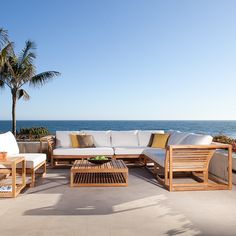 a couch and table on a patio overlooking the ocean with palm trees in the background