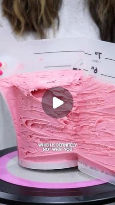 a pink cake sitting on top of a table next to a woman's hand