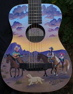 an acoustic guitar with cowboy scenes painted on the front and sides, featuring two men riding horses