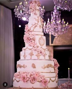 a three tiered wedding cake with pink flowers on the bottom and gold trimmings