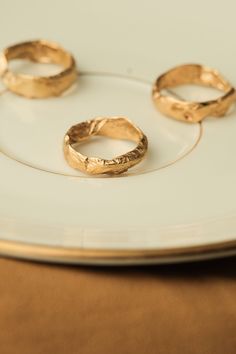 three gold rings sitting on top of a white plate next to each other in front of a brown table cloth