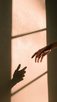 two hands reaching out towards each other in front of a window with light coming through