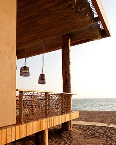 two lamps hanging from the side of a wooden structure on top of a sandy beach