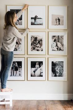 a woman is standing on a stool in front of a wall with many pictures hanging on it