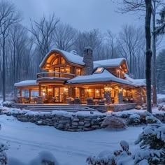 a large log cabin in the middle of a snowy forest with lights on it's windows