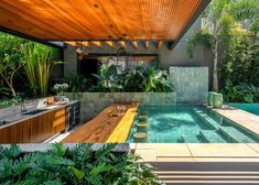 an outdoor kitchen next to a pool surrounded by greenery and wood planked roofing