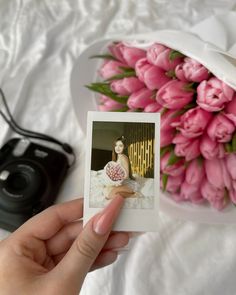 a person holding up a polaroid with pink flowers in the background and a camera