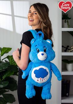 a woman holding a blue teddy bear backpack in front of her face and smiling at the camera