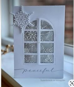 a white card with snowflakes on the window sill and words peaceful written in silver