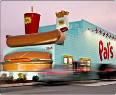 a large hot dog sitting on top of a bun next to a fast food restaurant