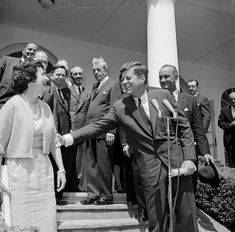 black and white photograph of two men shaking hands with other people in suits behind them