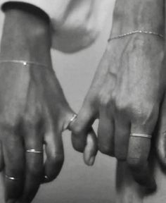 black and white photograph of two hands holding each other's fingers with rings on them