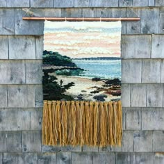 a tapestry hanging on the side of a wooden wall next to a building with water and clouds