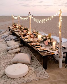 a long table set up on the beach with candles, flowers and plates in front of it