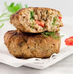 two meat patties stacked on top of each other with tomatoes and herbs in the background