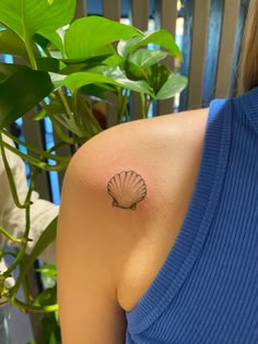 a woman's shoulder with a small tattoo of a seashell on her left arm