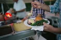 a person holding a plate with food on it while another person holds a spoon in their hand