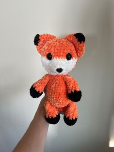 a hand holding a small crocheted orange and white stuffed animal with black eyes