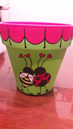 a green planter with ladybugs painted on it's sides sitting on a wooden table