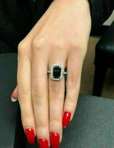 a woman's hand with red nail polish holding a black and white diamond ring