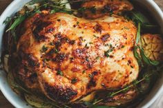 a cooked chicken in a white bowl with green garnish on the top and sides