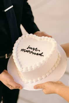 two people holding a heart shaped cake with the words just married written in black on it