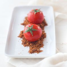 two tomatoes on a white plate with some seasoning