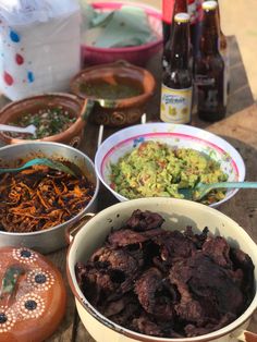 several bowls of food on a table with beer and condiments in the background