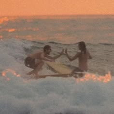 two surfers giving each other high fives in the ocean at sunset or dawn