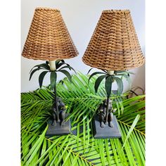 two lamps sitting next to each other on top of a table covered in palm leaves